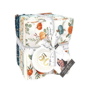 May include: A stack of fabric squares tied with a white ribbon printed with measurements. The fabric features a cream background with orange and teal pumpkins, green leaves, and red berries. A tag with the text "50 Years" is attached.