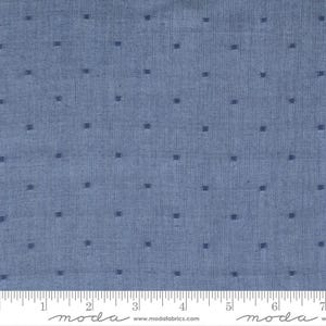 May include: Blue fabric with a repeating pattern of small, dark blue squares. The fabric has a textured appearance and a ruler is at the bottom. The word "moda" is printed on the ruler.