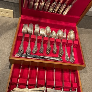 May include: A wooden silverware chest with a red velvet interior, filled with an assortment of silver forks, spoons, and knives. The silverware has ornate handles and is arranged neatly in the chest.