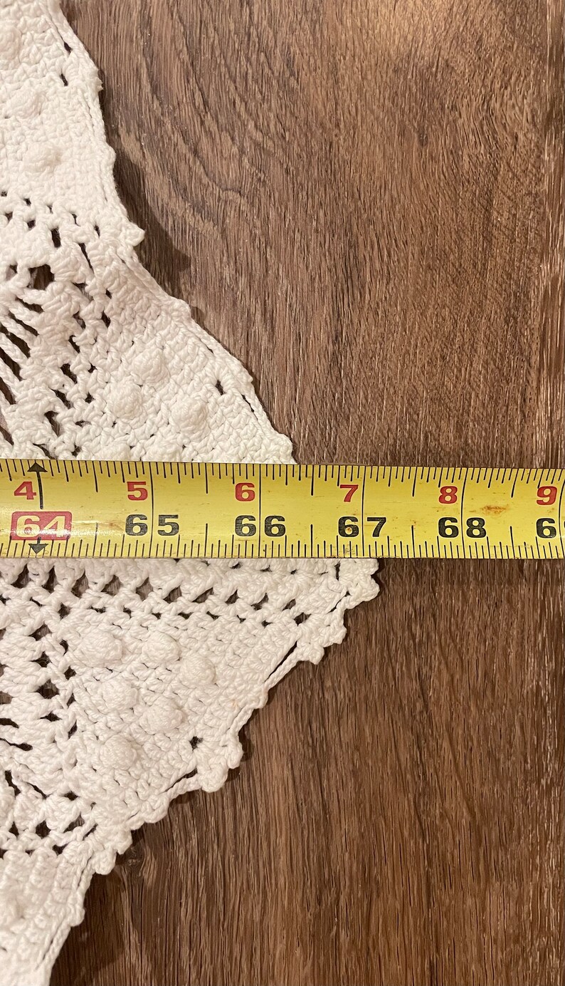 May include: A white, crocheted doily with a scalloped edge, partially visible against a wooden surface. A yellow measuring tape shows a length of approximately 64 to 69 inches.