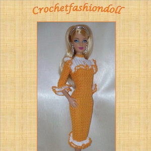 Può includere: Un abito arancione all'uncinetto con bordi bianchi, indossato da una bambola con capelli biondi e occhi azzurri. L'abito ha un collo e un orlo a balze. La bambola indossa scarpe argentate. Il testo "By Anna Rita" e "Orange Cloud" è visibile nell'immagine.