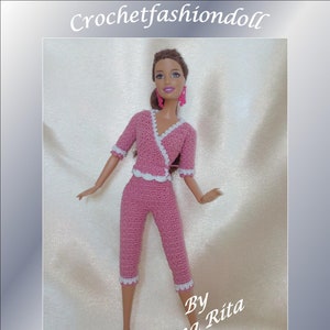 Pode incluir: Um conjunto de pijama de crochê rosa com detalhes em branco para uma boneca. A boneca está usando o pijama e tem cabelo castanho e brincos rosa. O texto "By Anna Rita" e "Pink Pajamas" é visível na imagem.