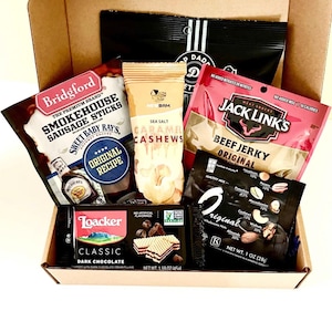 May include: A gift box filled with various snacks. The box contains a bag of Bridgford Smokehouse Sausage Sticks, a bag of Sea Salt Caramel Cashews, Jack Link's Beef Jerky, a dark chocolate wafer bar, and a bag of mixed nuts.