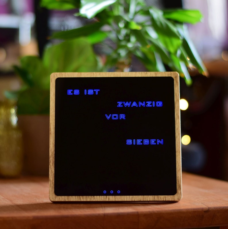 May include: A wooden clock with a black face and blue digital display showing the time "ES IST ZWANZIG VOR SIEBEN".