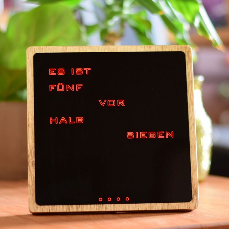 May include: A wooden framed clock with a black face and red digital display. The clock reads "ES IST F&Uuml;NF VOR HALB SIEBEN".