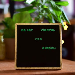 May include: A wooden framed chalkboard with the text "Es ist Viertel vor Sieben" written in green.