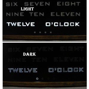 Puede incluir: Un reloj de volteo negro con n&uacute;meros blancos muestra la hora como las 12 en punto. El reloj tiene un marco de madera y est&aacute; iluminado en dos modos diferentes: "light" y "dark".