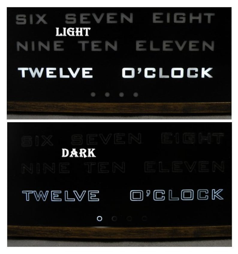 Puede incluir: Un reloj de volteo negro con n&uacute;meros blancos muestra la hora como las 12 en punto. El reloj tiene un marco de madera y est&aacute; iluminado en dos modos diferentes: "light" y "dark".