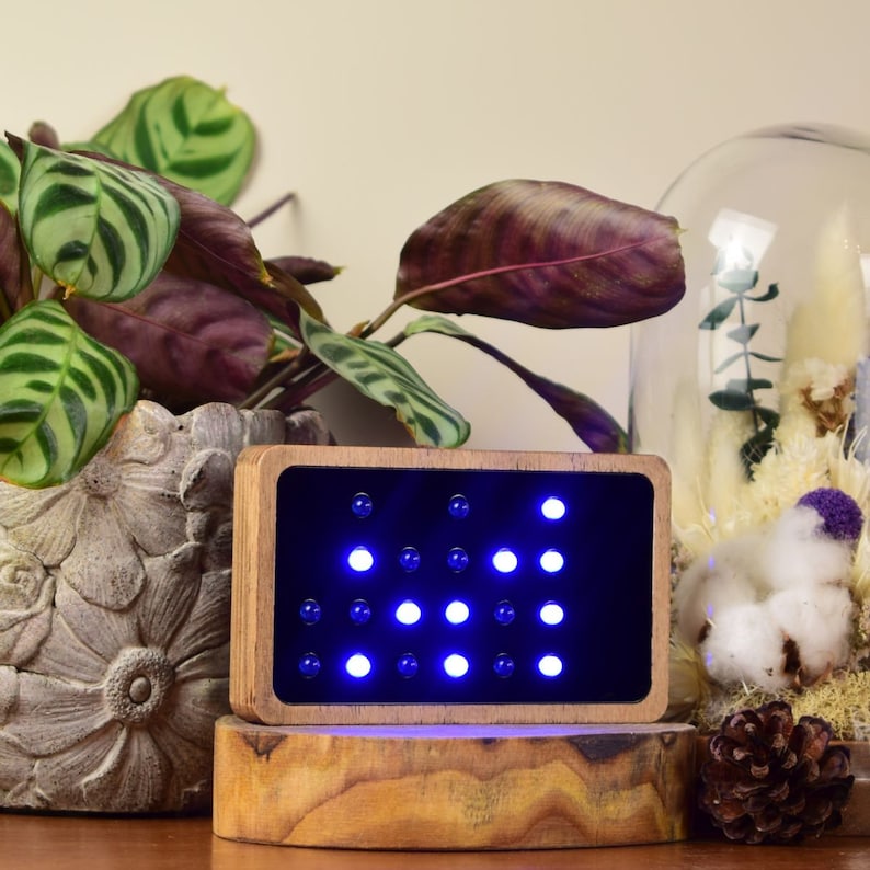 Op de afbeelding: Een houten frame met een zwarte achtergrond en een raster van blauwe LED-lampjes. Het frame staat op een houten oppervlak.