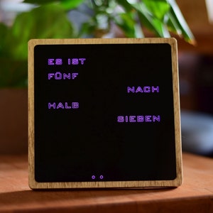 May include: A wooden clock with a black face and purple digital display. The clock reads "ES IST F&Uuml;NF NACH HALB SIEBEN".