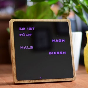 May include: A wooden framed digital clock with a black display showing the time in German as "Es ist f&uuml;nf nach halb sieben".