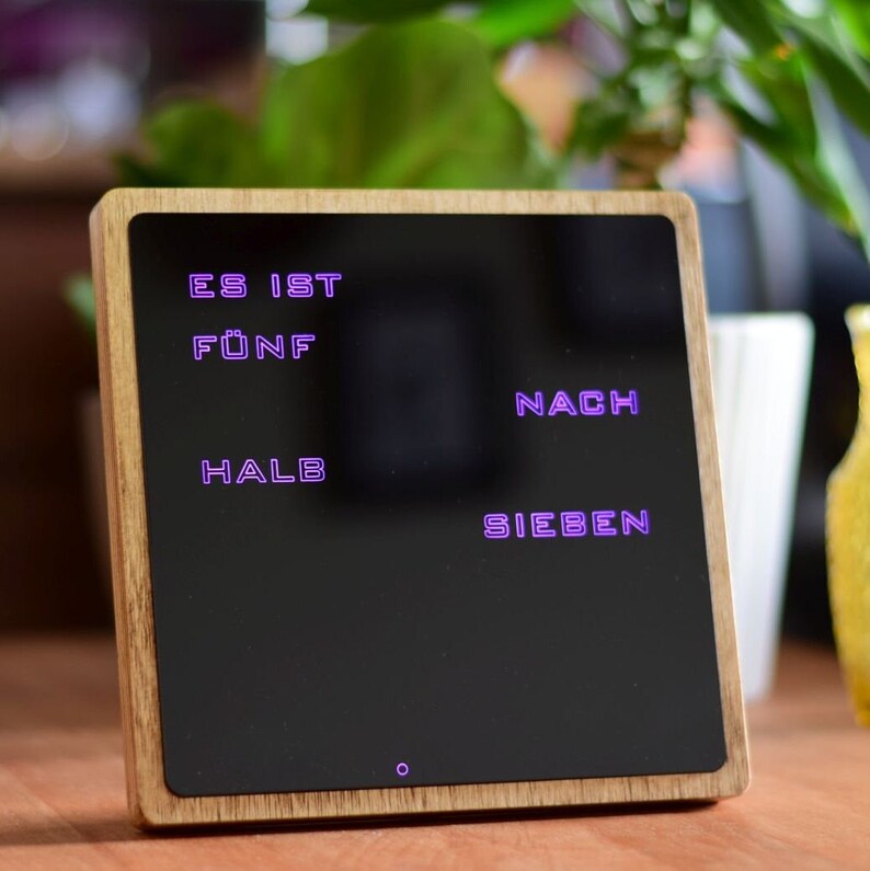 May include: A wooden framed digital clock with a black display showing the time in German as "Es ist f&uuml;nf nach halb sieben".