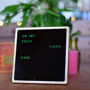 May include: A wooden framed clock with a black face and green digital numbers that read "ES IST F&Uuml;NF NACH DREI".