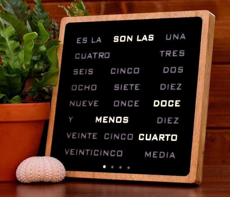 Puede incluir: Un letrero de madera con marco negro y texto blanco sobre fondo negro. El texto dice "ES LA SON LAS UNA CUATRO TRES SEIS CINCO DOS OCHO SIETE DIEZ NUEVE ONCE DOCE Y MENOS DIEZ VEINTE CINCO CUARTO VEINTICINCO MEDIA".