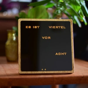 May include: A wooden clock with a black face and white text that reads "Es ist Viertel vor Acht".