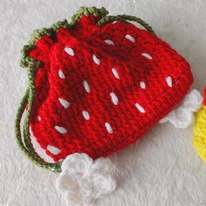 May include: Two crocheted pouches: one shaped like a red strawberry with white seeds and green accents, the other yellow with a brown design and a red bow. These handmade pouches are perfect for small gifts.