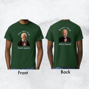 Può includere: T-shirt verde scuro con una grafica frontale di un uomo che tiene una bacchetta, con il testo "Guess who's back, back again". Il retro della maglietta presenta lo stesso uomo con il testo "Draco's back, tell a friend".
