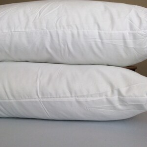 May include: Two white pillows stacked on top of each other. The pillows are made of a soft, white fabric and have a smooth, even surface.