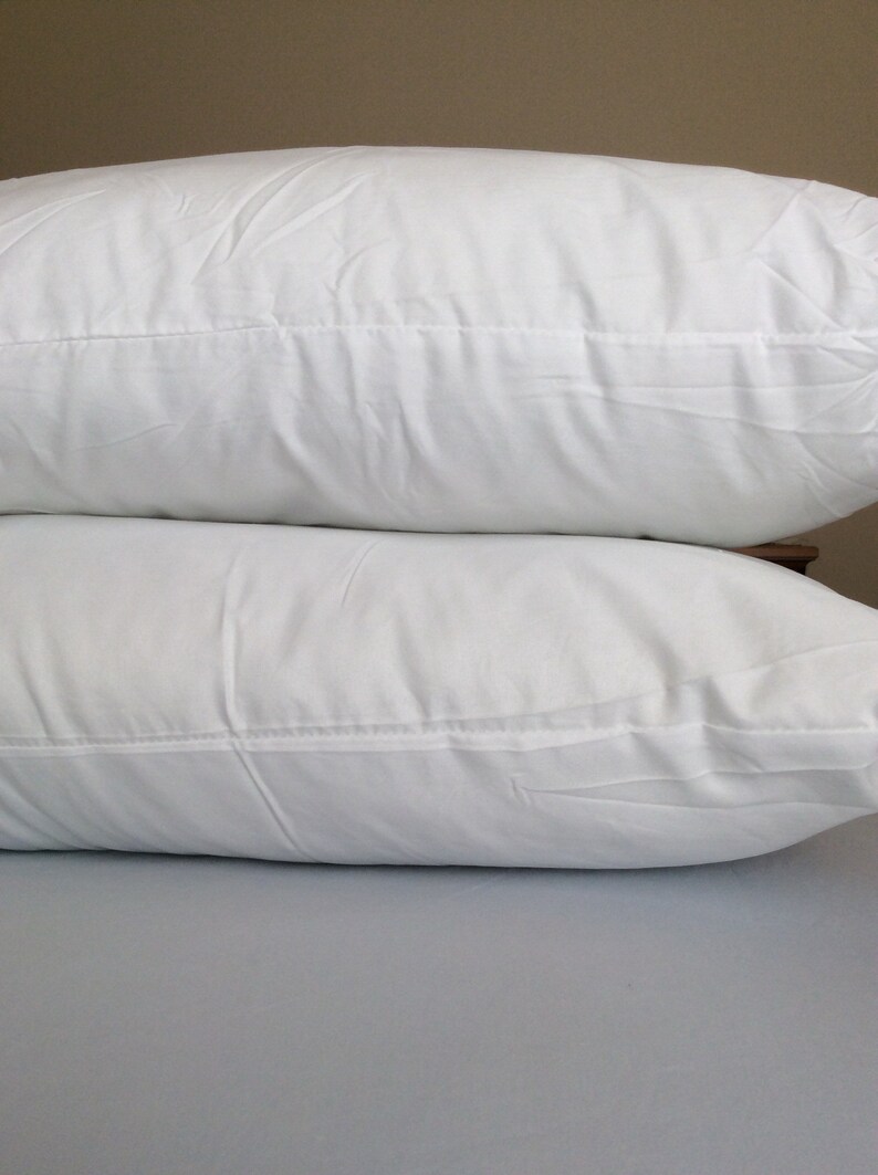 May include: Two white pillows stacked on top of each other. The pillows are made of a soft, white fabric and have a smooth, even surface.
