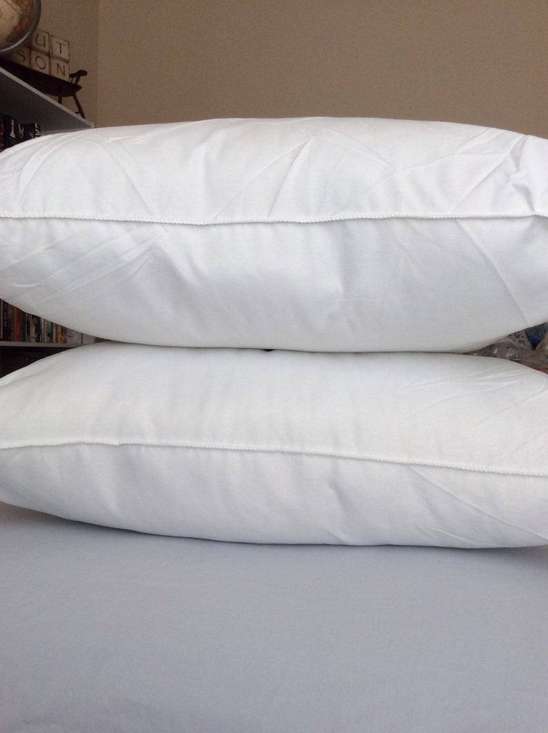 May include: Two white pillows stacked on top of each other. The pillows are made of a soft, white fabric and have a simple, clean design.