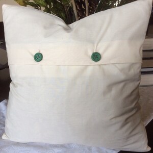 May include: A white pillow with two green buttons. The pillow is on a white lace tablecloth.