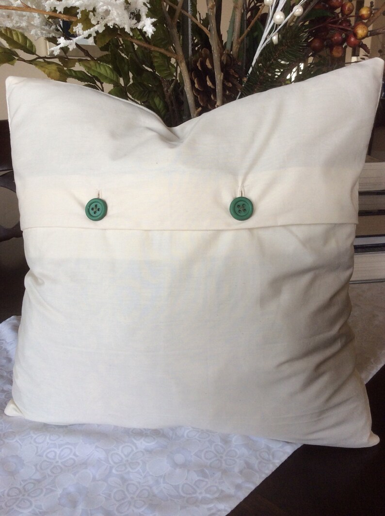 May include: A white pillow with two green buttons. The pillow is on a white lace tablecloth.