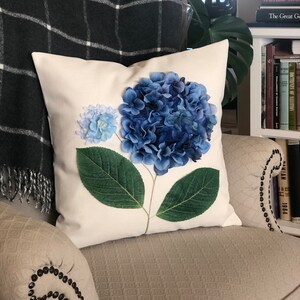 May include: A white pillow with a blue and green hydrangea flower pressed onto the fabric.