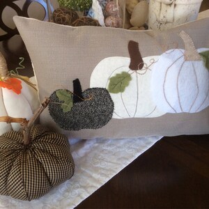 May include: A rectangular cushion featuring appliqu&eacute;d white and dark grey pumpkins. Two fabric pumpkins with stems and leaves are in front of the cushion. The pumpkins are white, and black and white checked.