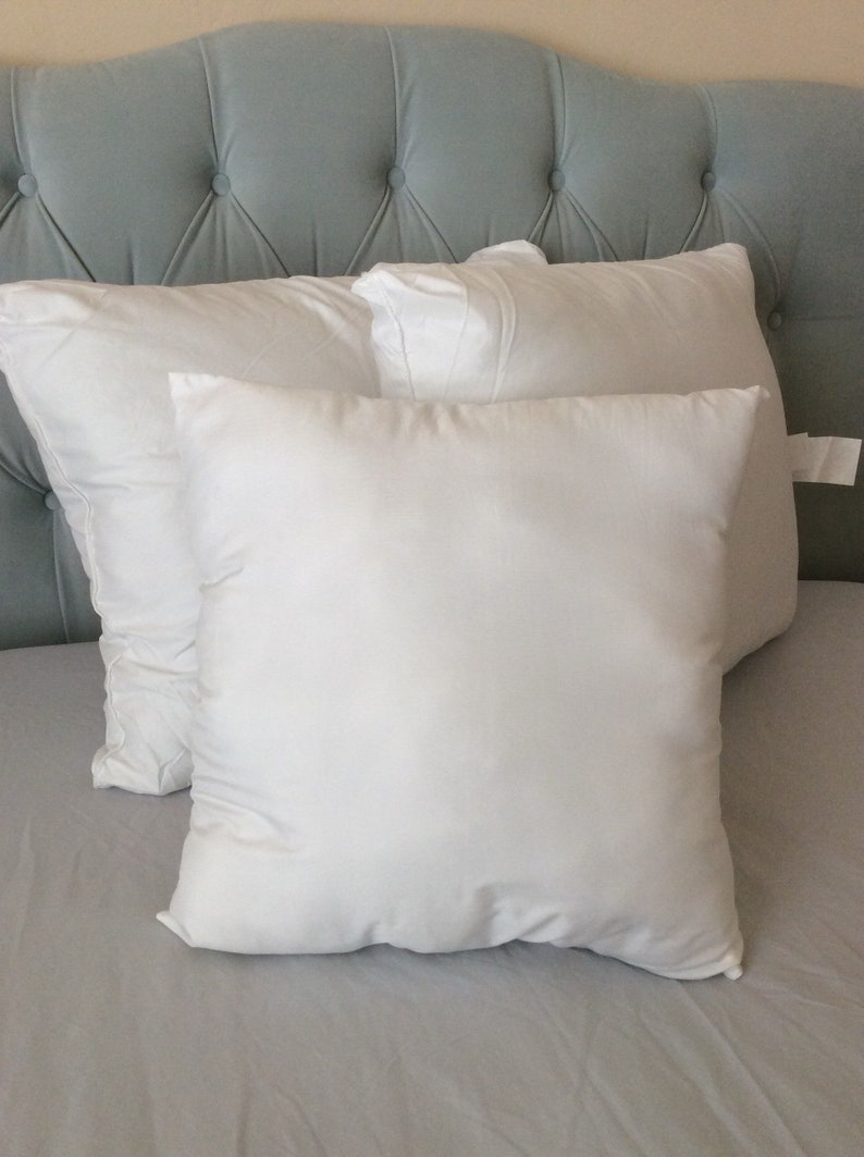 May include: Three white pillows on a light gray bed with a light blue tufted headboard.