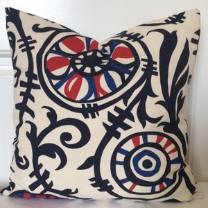 May include: Square cushion with a cream-coloured background and a striking pattern in navy blue, red, and blue. The design features stylised floral and geometric shapes, creating a bold visual contrast. A home decor item.