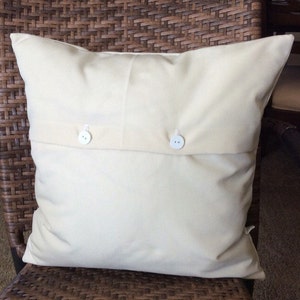May include: A white pillow with two white buttons on the back. The pillow is sitting on a brown wicker chair.
