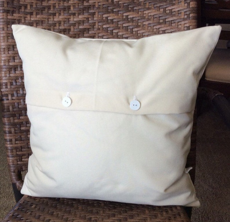 May include: A white pillow with two white buttons on the back. The pillow is sitting on a brown wicker chair.