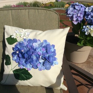 May include: A white pillow with a blue and purple hydrangea flower design. The pillow is on a green chair.