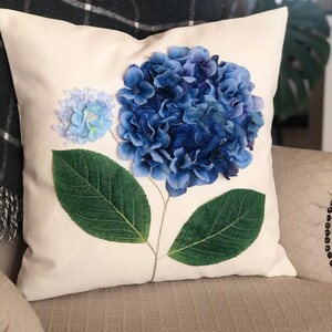 May include: A white pillow with a blue and green hydrangea flower design. The flower is made of fabric and has a realistic appearance.
