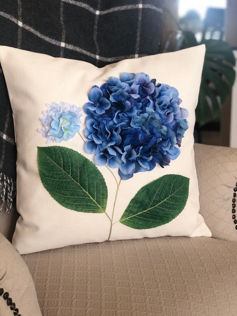 May include: A white pillow with a blue and green hydrangea flower design. The flower is made of fabric and has a realistic appearance.