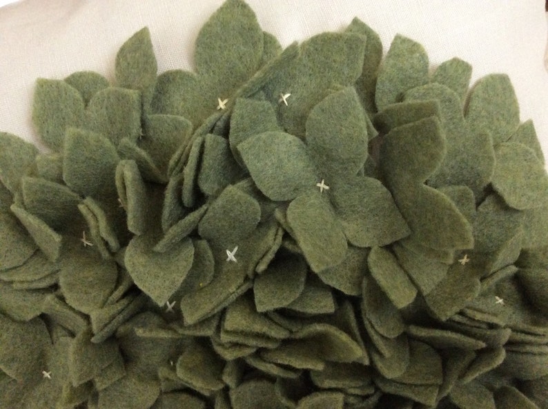 May include: A close-up of a green felt flower arrangement. The flowers are made of individual felt petals sewn together to create a 3D effect.