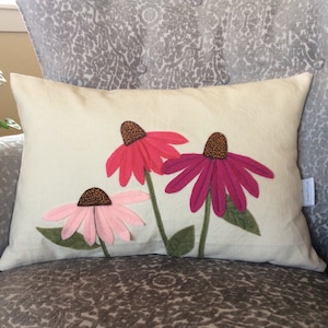 May include: A white pillow with three felt flowers appliqued on it. The flowers are pink, red, and purple with brown centers.