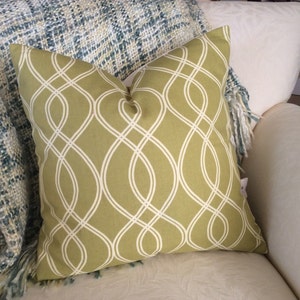 May include: A green and white patterned throw pillow with a woven design. The pillow is on a white couch with a blue and white throw blanket.
