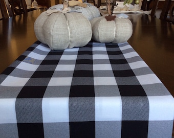 Puede incluir: Un camino de mesa a cuadros blanco y negro con tres calabazas decorativas sobre una mesa de madera. Las calabazas están hechas de tela y tienen un estilo rústico y de granja.
