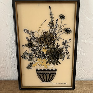May include: A framed floral still life featuring a vase filled with stylized flowers in shades of gray, black, and yellow. The artwork is set against a cream-colored background and framed in a black rectangular frame. The artist's signature, "Smith Frederick," is visible.
