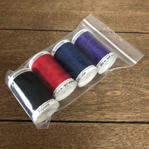 May include: Four spools of Gütermann thread in black, red, blue, and purple. Each spool is labeled with the brand name, "Gütermann", and the length of the thread, "500 m - 547 yds".