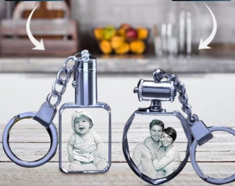 Può includere: Due portachiavi di cristallo con anelli e catene in metallo argentato. Un portachiavi presenta un cristallo quadrato con una foto di una bambina. L'altro portachiavi presenta un cristallo esagonale con una foto di una coppia.