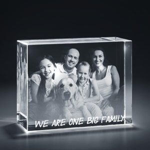 May include: A 3D crystal cube with a family photo inside. The photo shows a family of four with a dog. The text "WE ARE ONE BIG FAMILY" is engraved on the bottom of the cube.
