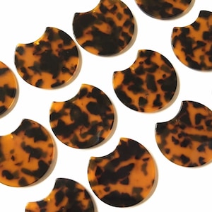 May include: A collection of 10 brown and black tortoise shell patterned half-circle acrylic resin shapes. The shapes are arranged in a staggered pattern on a white background.