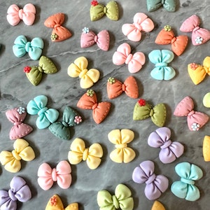May include: Assortment of colorful fabric bows with various patterns and designs. The bows are made of different materials and have a variety of textures.