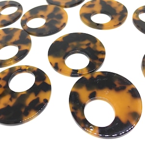 May include: A collection of tortoise shell-patterned acrylic pendants. The pendants are various shapes, including oval and circular, with a hole in the center. The color scheme is a mix of dark brown and amber.
