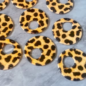 May include: Eight round, brown and black leopard print acrylic circles with a hole in the center.