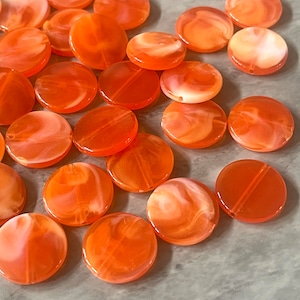 May include: A collection of round, orange and white marbled plastic beads. The beads have a swirl pattern and are perfect for jewelry making.