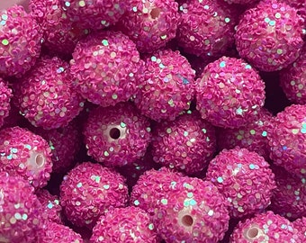 Op de afbeelding: Close-up van een stapel roze kralen met een getextureerd, met pailletten bezet oppervlak. De kralen zijn rond met een gat in het midden, geschikt om te rijgen. De pailletten hebben een iriserende glans.