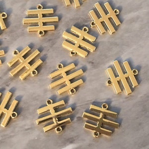 May include: A group of 12 gold-colored metal charms, each featuring a geometric design of five horizontal bars. The charms have two holes at the top for attaching to jewelry or other crafts.